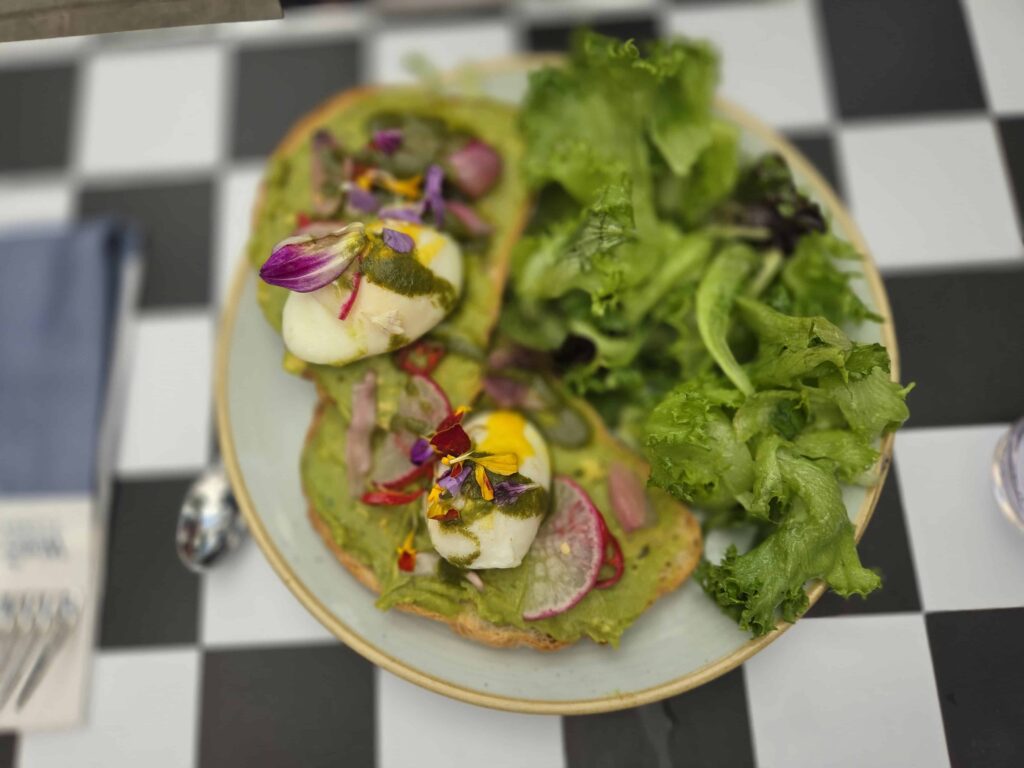 avacado toast and salad topped with a soft boiled egg and eatable flowers